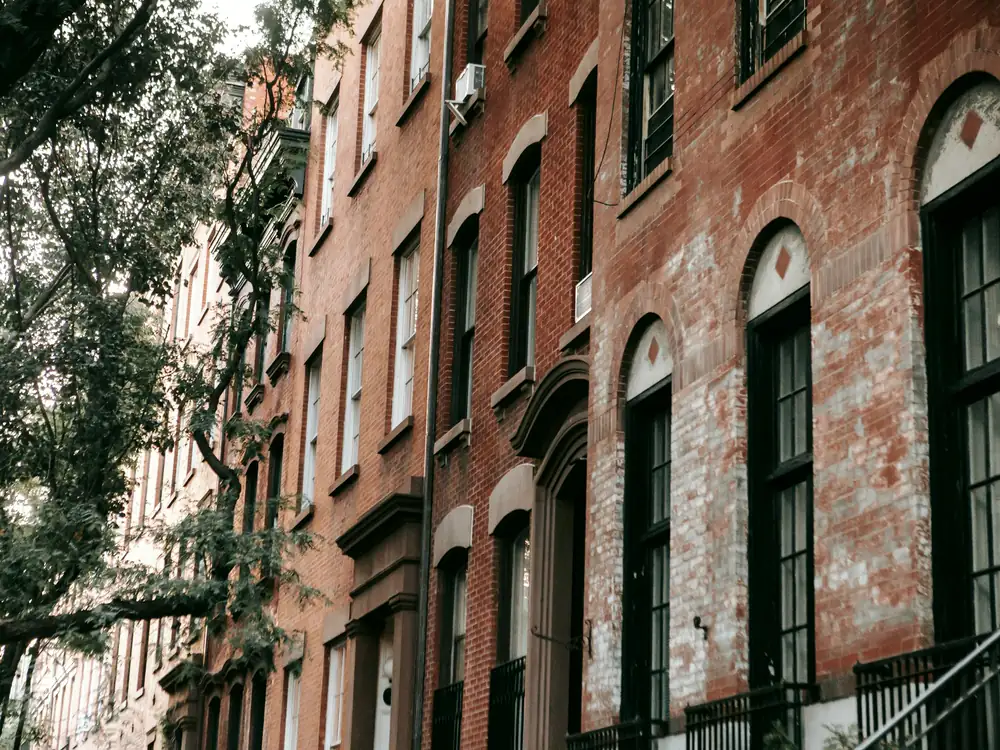 A tall brick apartment building with arched window heads and black iron railings, framed by a street tree.