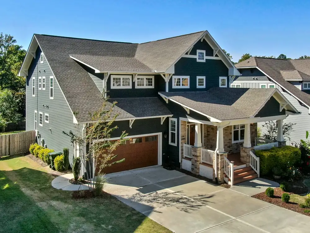 A dark blue Craftsman house with a stone-based front porch, a wood garage door and a landscaped front yard.