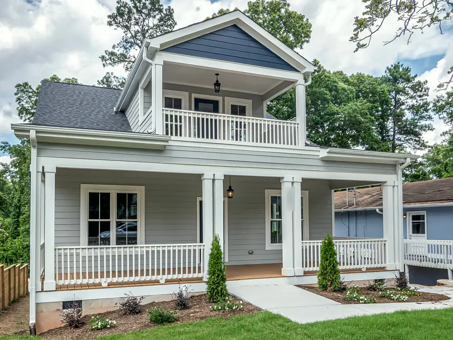 A grey two-storey house with a deep front porch and an upstairs balcony porch, seen from the side of a small front lawn.